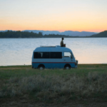 A man sitting on a van in front of a lake