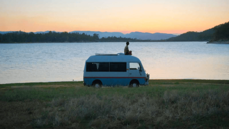A man sitting on a van in front of a lake
