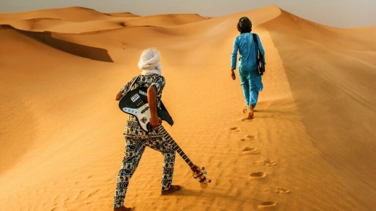 Desert blues, guitarists walking along a dune