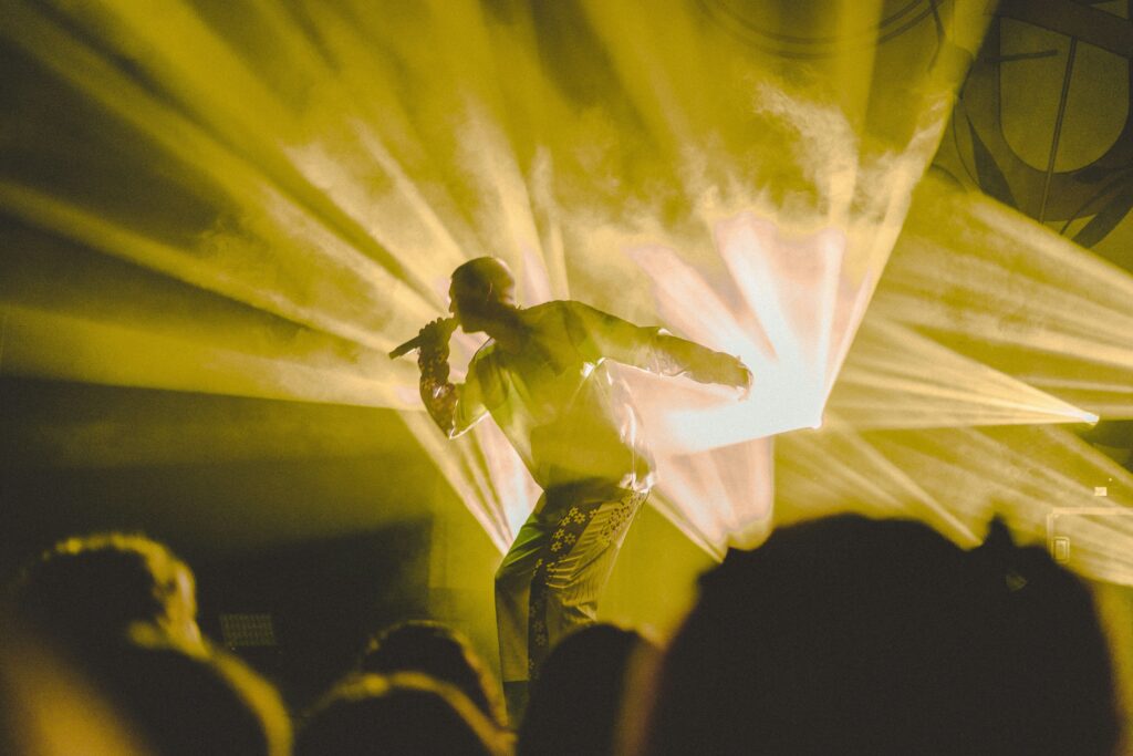 Artist onstage with yellow lighting shining behind.