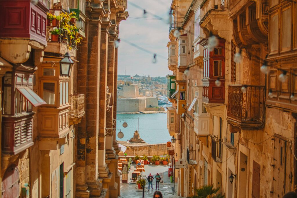 Narrow side streets of Valletta with classic Maltese balconies and the harbor in the background.