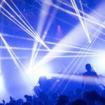 DJ set with blue and white lighting, people raising their arms.