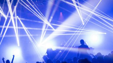 DJ set with blue and white lighting, people raising their arms.
