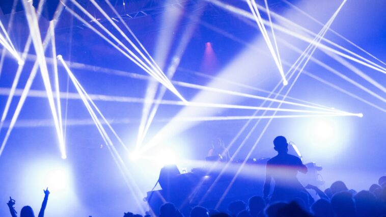 DJ set with blue and white lighting, people raising their arms.