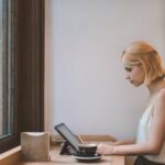 Woman working from a cafe on a laptop with a coffee next to her.