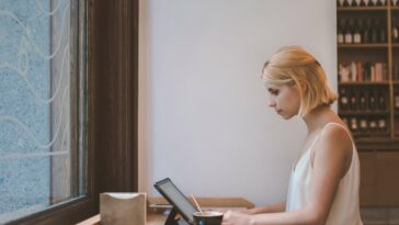 Woman working from a cafe on a laptop with a coffee next to her.