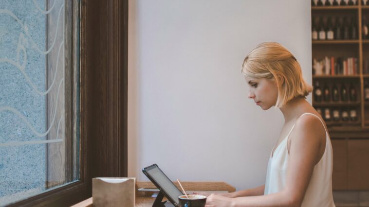 Woman working from a cafe on a laptop with a coffee next to her.