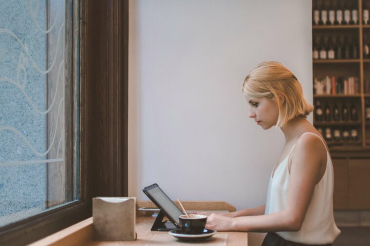 Woman working from a cafe on a laptop with a coffee next to her.