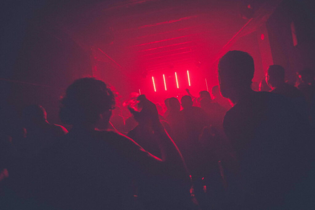 Photo from the back of a club with red neon lights and people dancing.