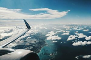 View from an airplane overlooking a coastline with sun and clouds.