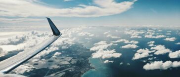 View from an airplane overlooking a coastline with sun and clouds.
