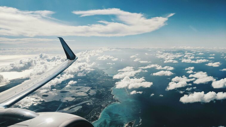 View from an airplane overlooking a coastline with sun and clouds.